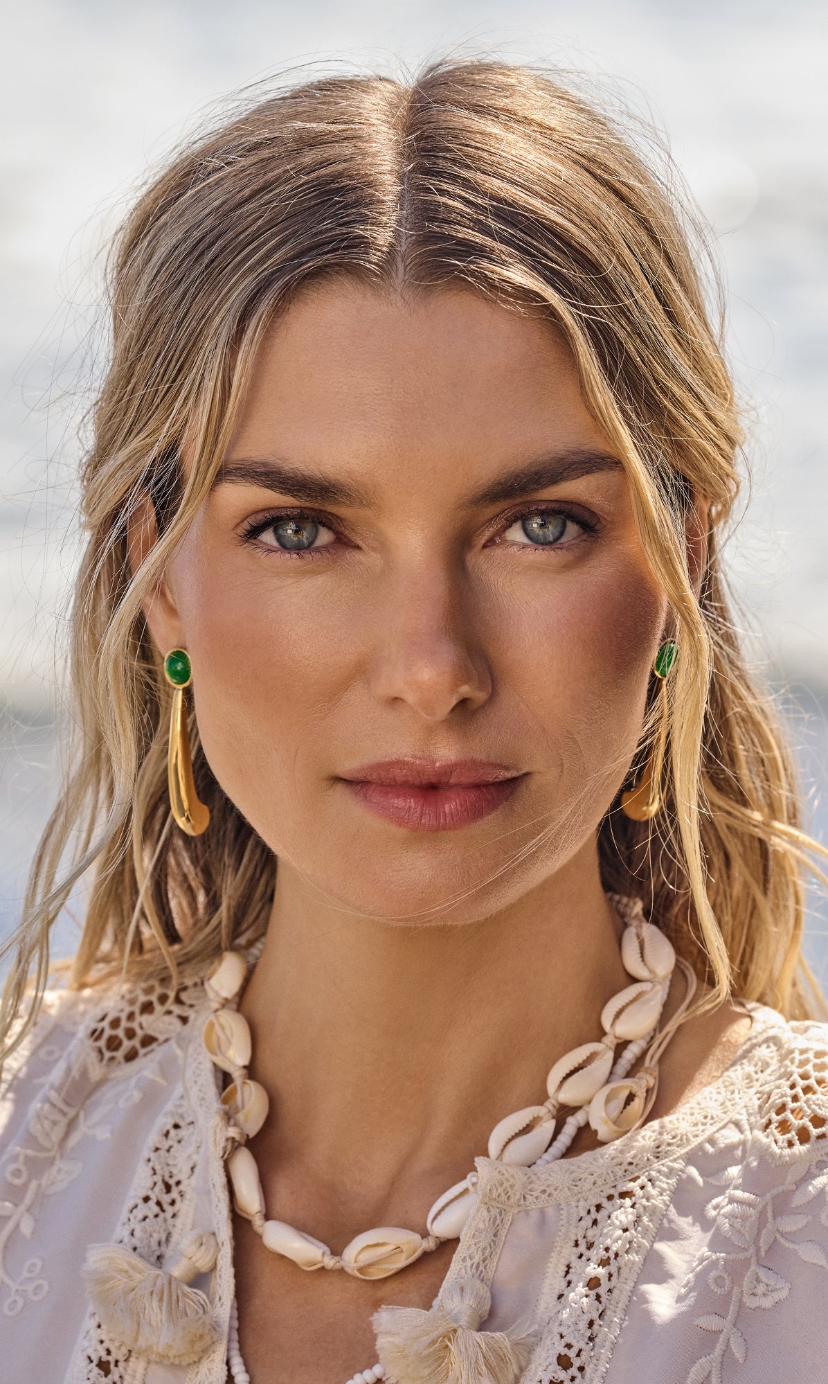 Person wearing earrings and a shell necklace by water.