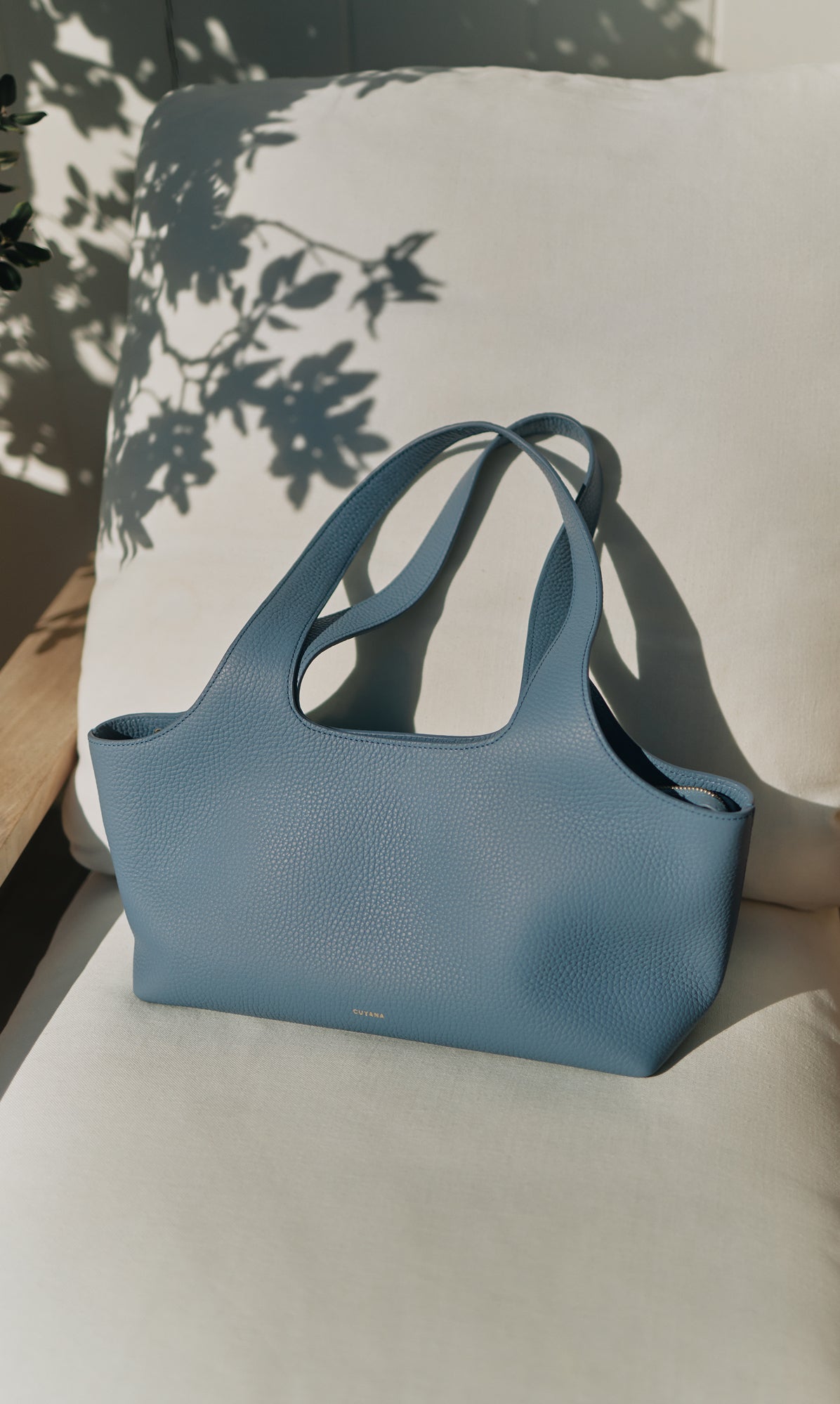 Handbag sitting on a cushioned chair with plant shadows in background.