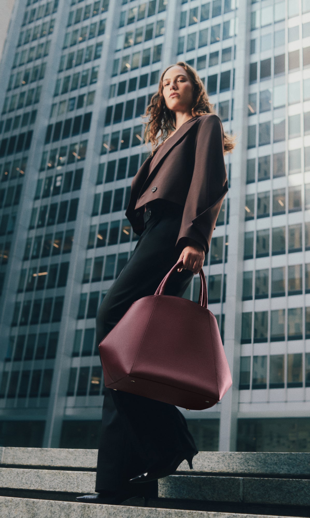 Person standing on steps holding a large bag, with tall building in background.