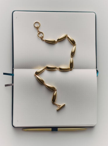 Open notebook with an abstract-shaped necklace and a pen.