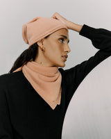 Woman in a beanie and sweater holding her hand on her head.