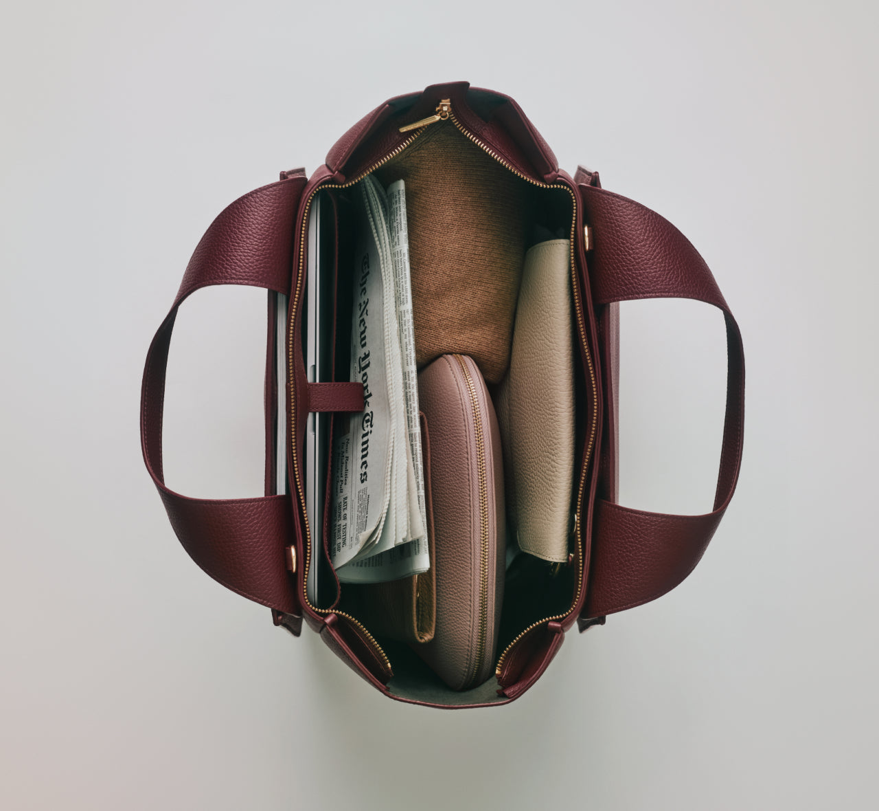 Open handbag containing a newspaper and two pouches.