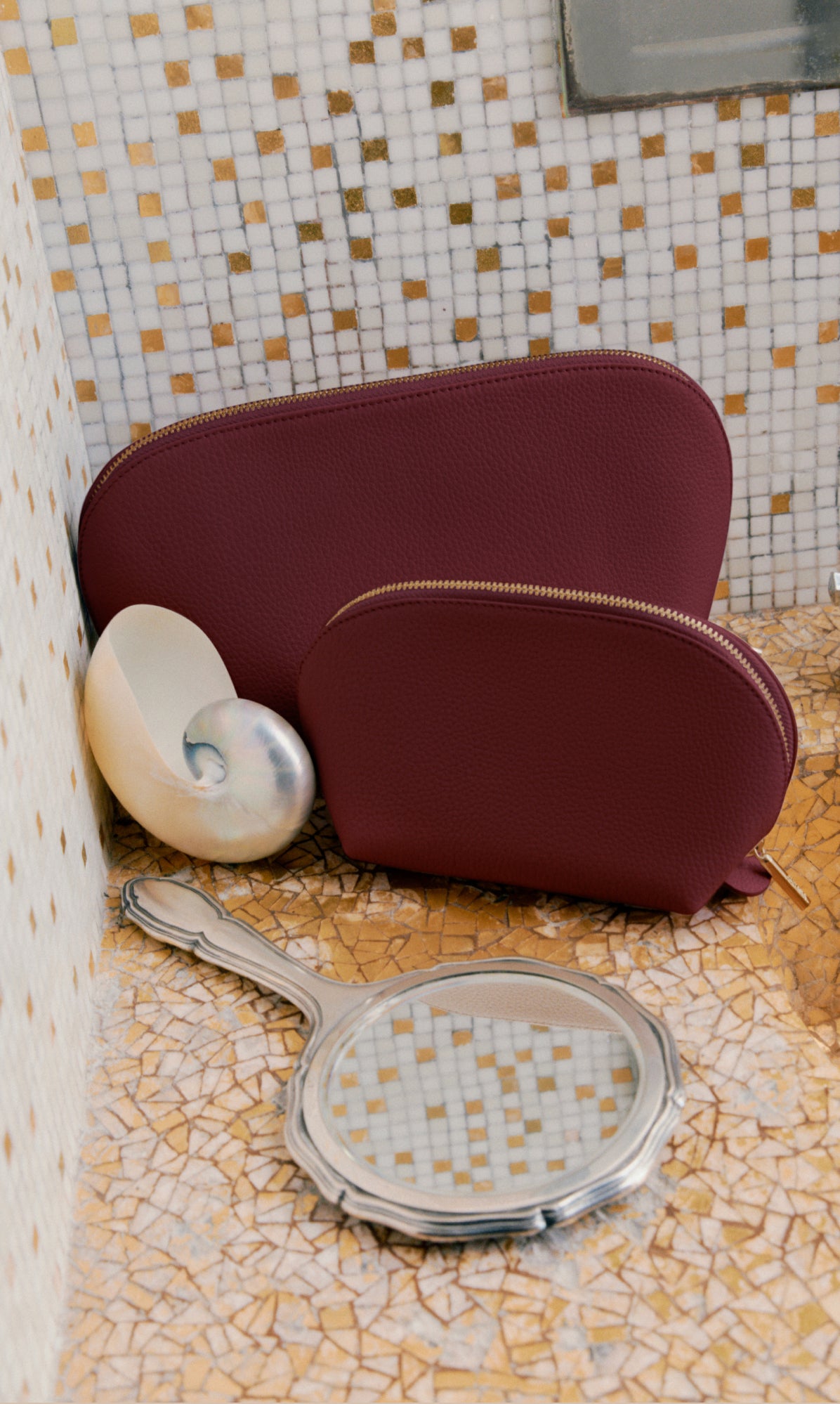 Two pouches next to a seashell and hand mirror on a mosaic surface.