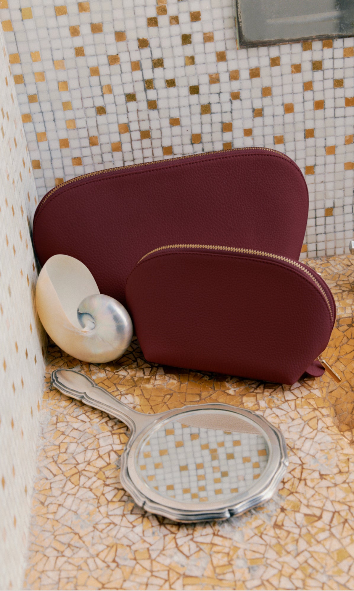 Two zippered pouches, a seashell, and a handheld mirror on a tiled surface.