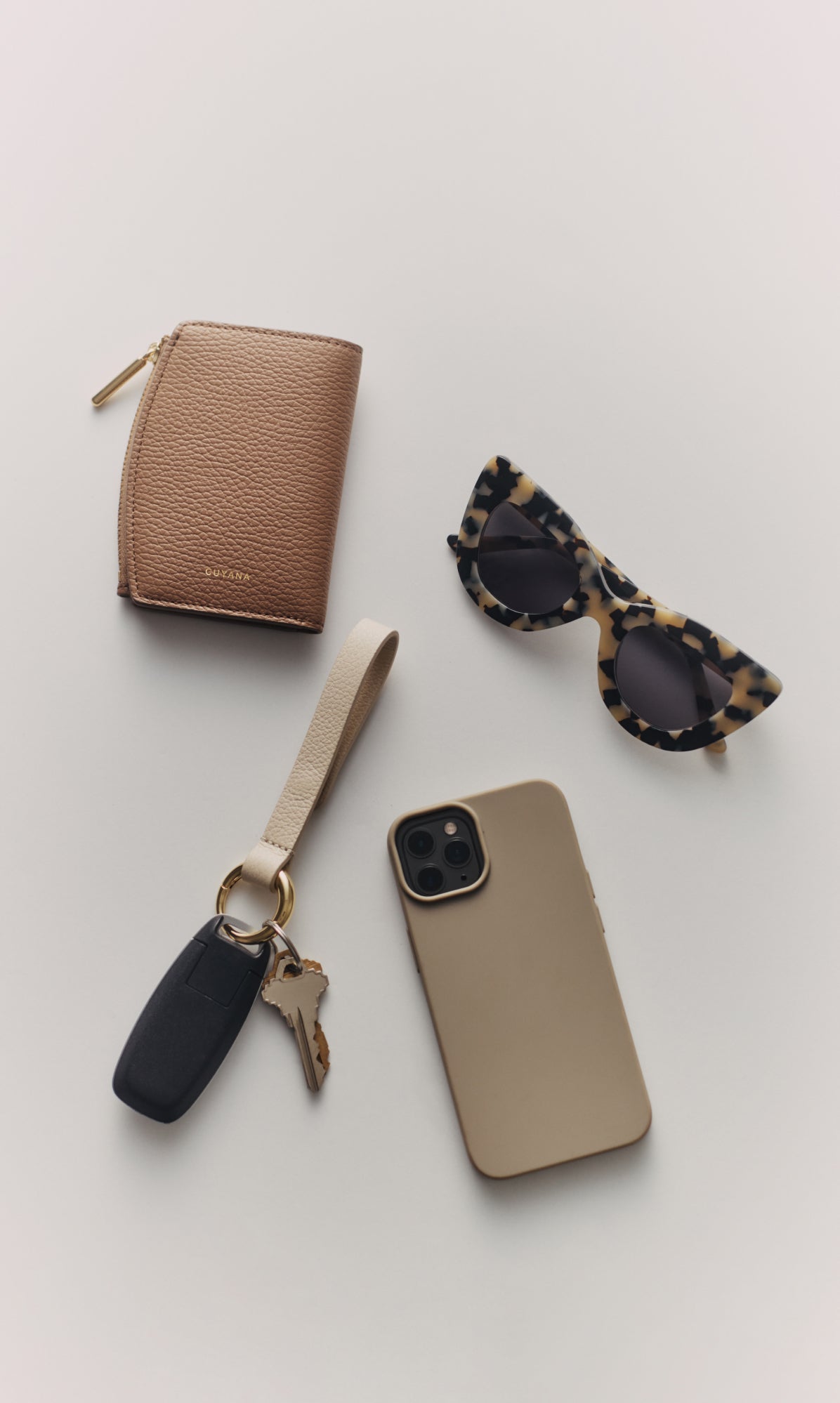 Wallet, sunglasses, phone with keychain, and keys on a flat surface.