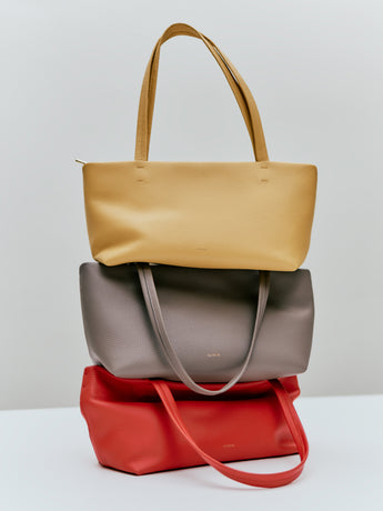 Three stacked tote bags with handles on a surface
