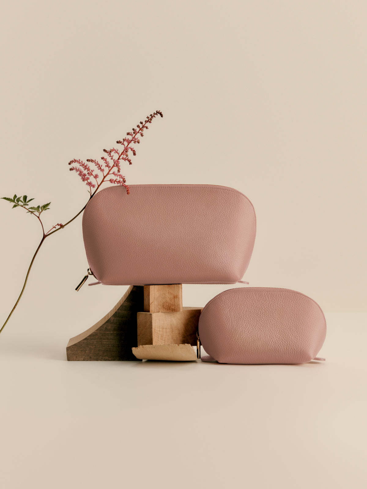 Two purses on a pedestal with a plant beside them.