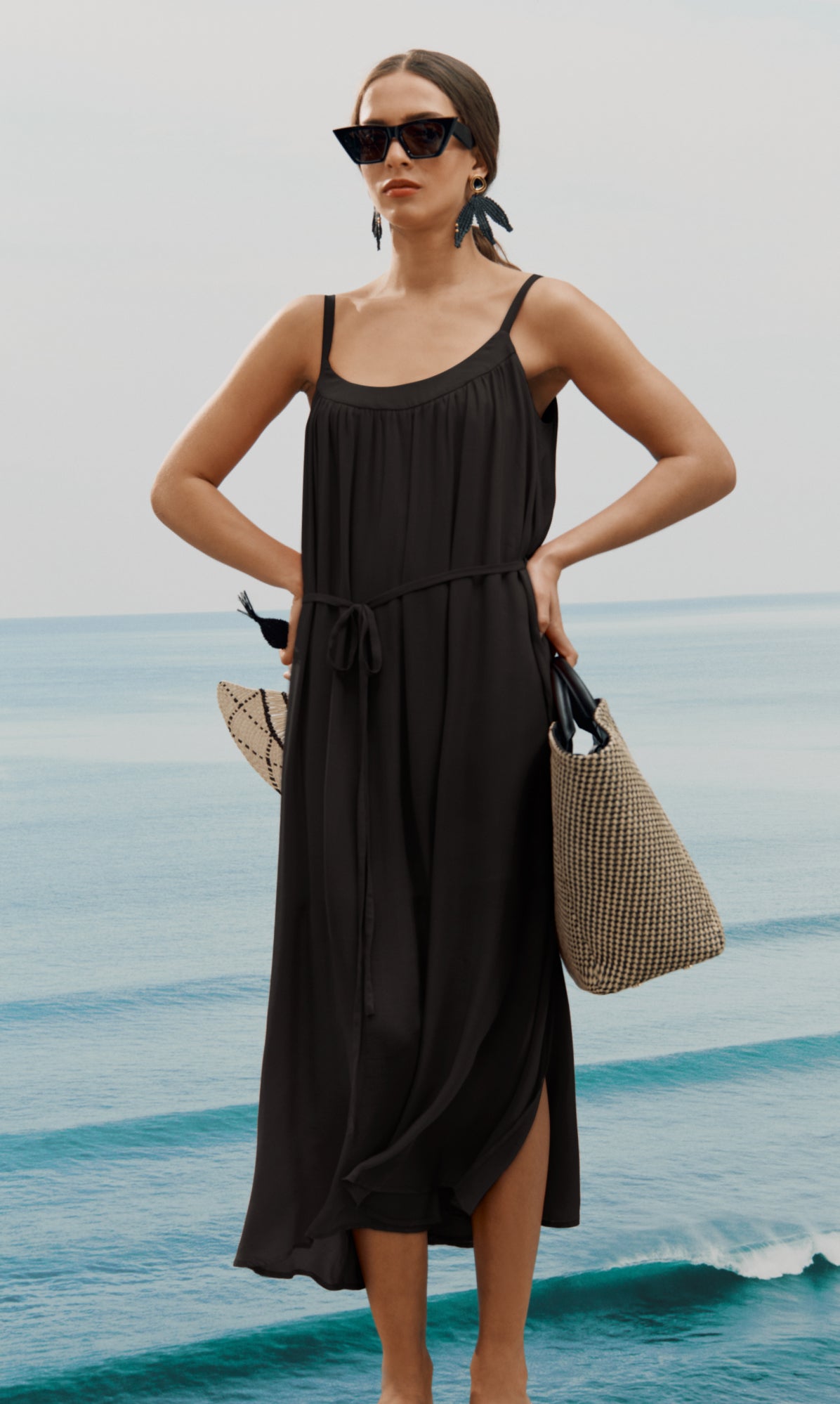 Person wearing dress holding woven tote bag by the sea.
