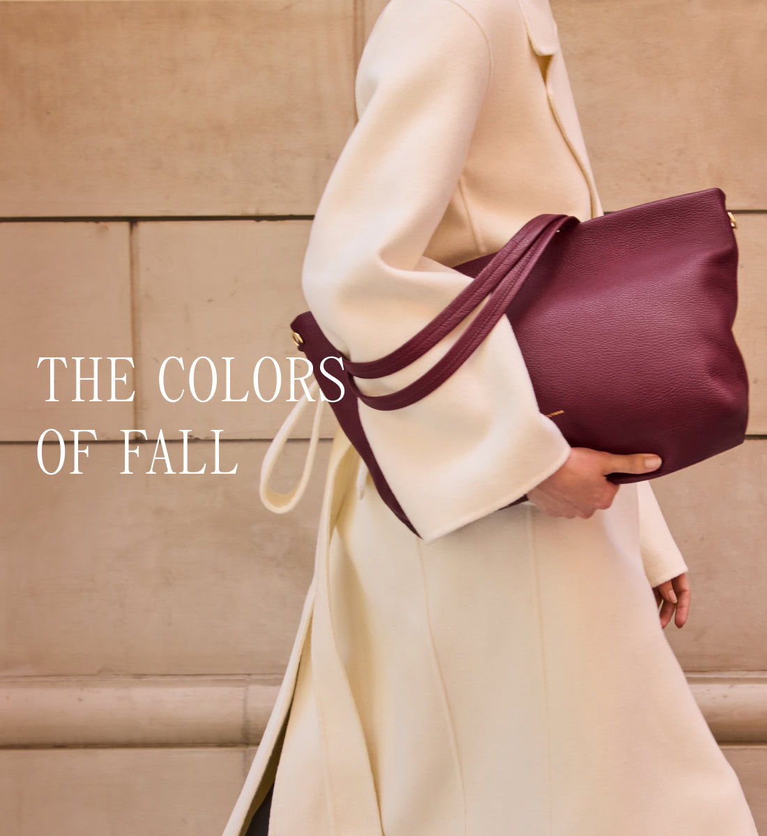 Person holding a large handbag while walking past a wall.