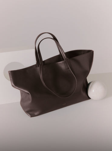 Tote bag with round handle next to a small sphere object on a flat surface.