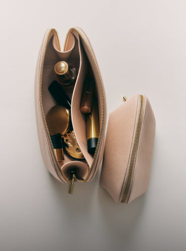 Open cosmetic bag with makeup items inside, next to a closed pouch.