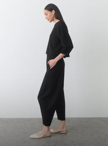 Person in side profile wearing a loose-fitting top and pants with flat shoes.