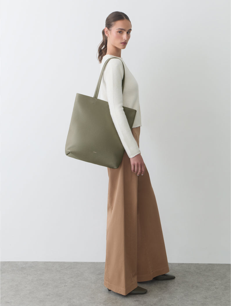 Person holding a large tote bag, wearing a sweater and wide-leg pants, standing sideways.