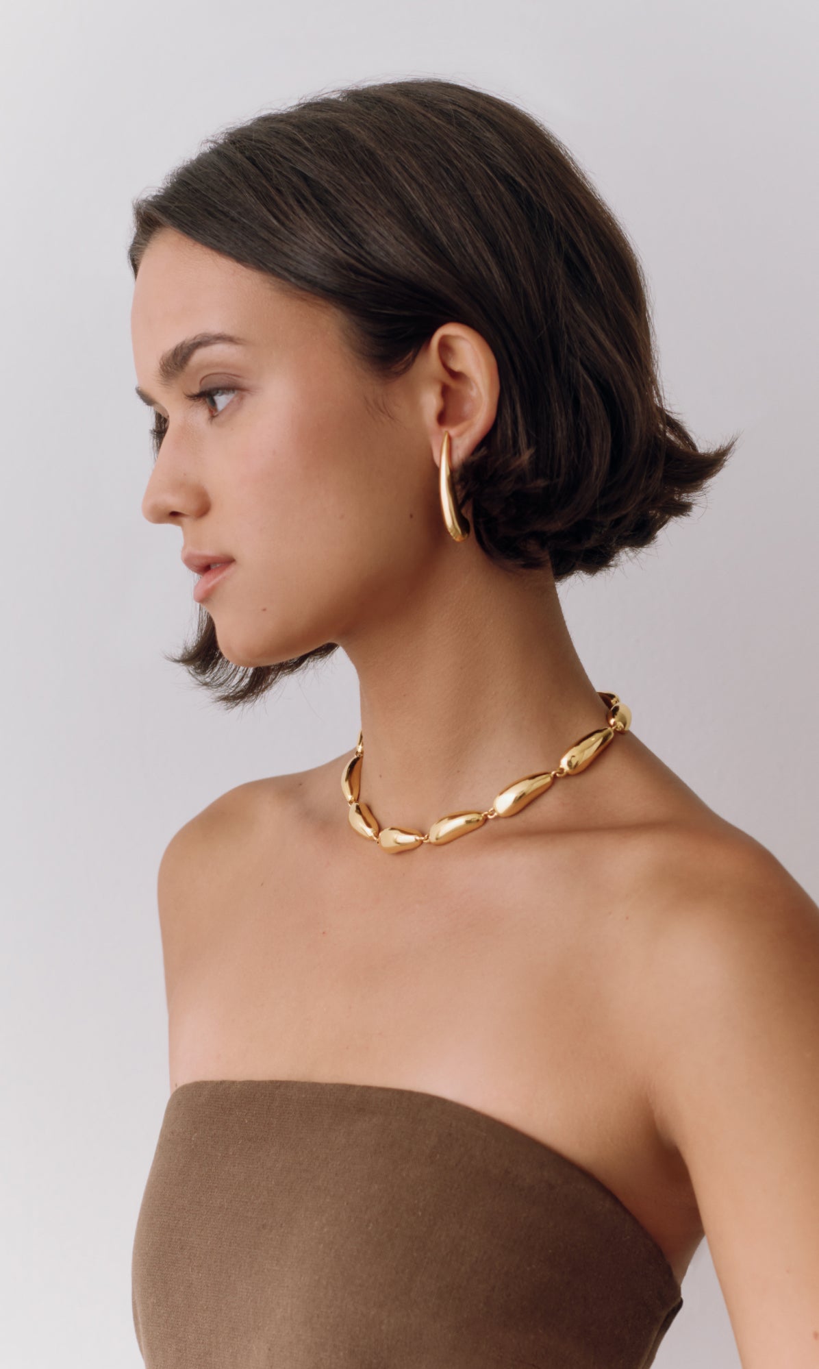 Woman wearing gold hoop earrings and necklace, facing sideways.