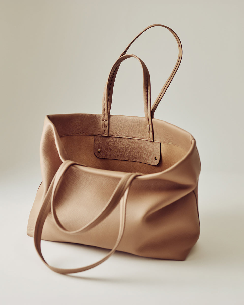 A spacious handbag with two handles on a plain surface.