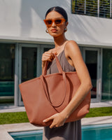 Woman in a dress holding a large tote bag by a poolside.
