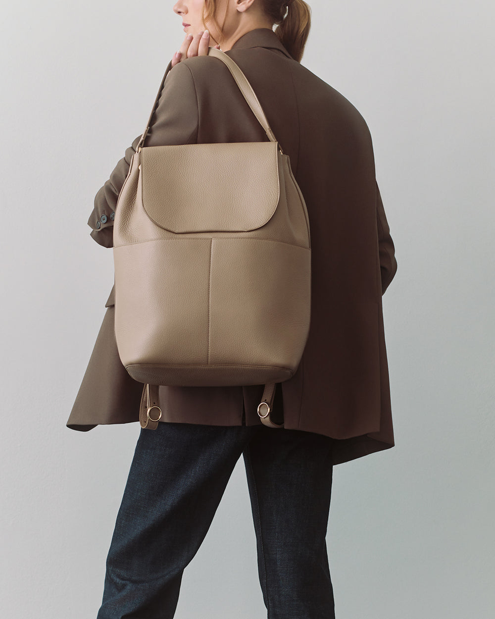 Person holding a backpack over their shoulder, wearing a blazer and jeans.