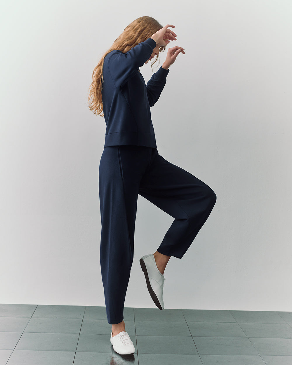 Person in a two-piece outfit, standing on one leg with arms raised.