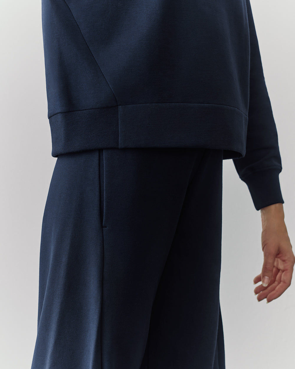 Person in a relaxed fit outfit, cropped image of torso and hand.