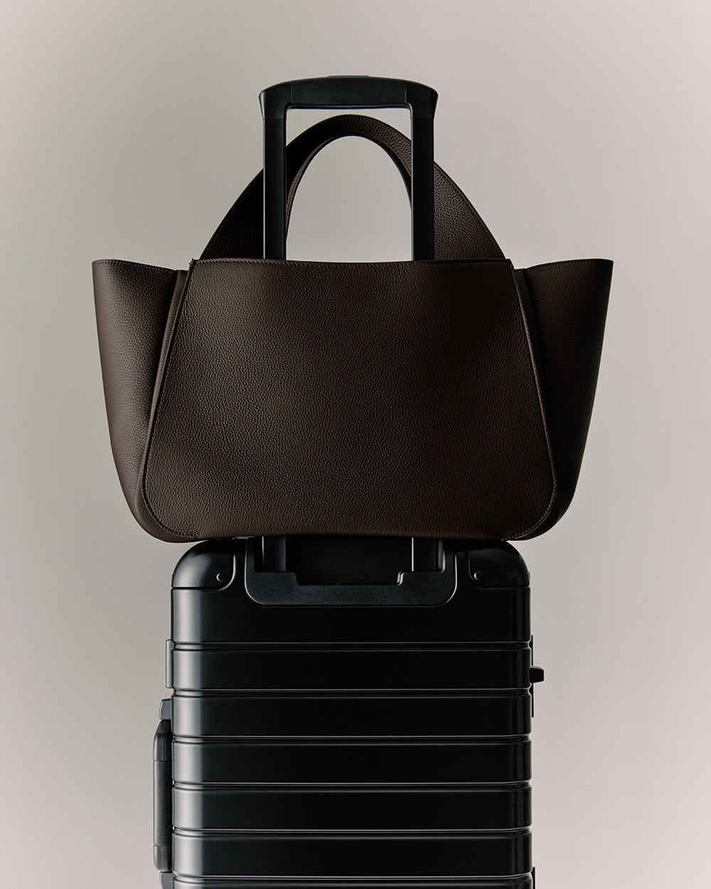 Tote bag resting on a wheeled suitcase handle.