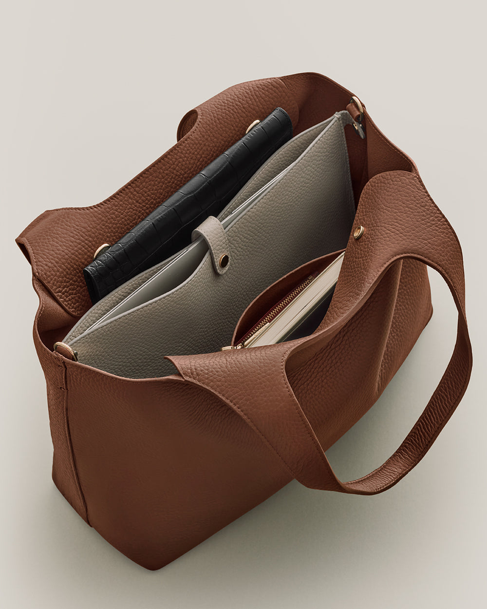 Open handbag with various items inside, including a tablet and a zippered pouch.