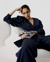 Woman sitting on a chair in a stylish outfit with hand on head.