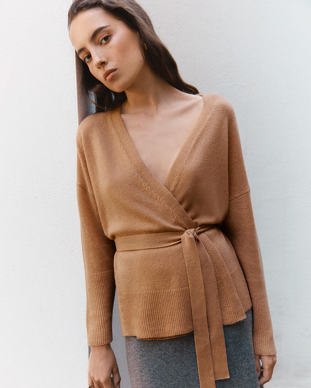 Woman posing in a wrap-style top against a plain background.
