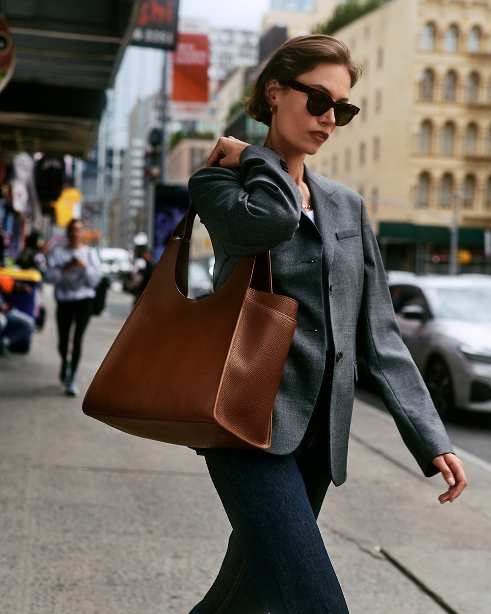 Person walking on city sidewalk with large tote bag over shoulder