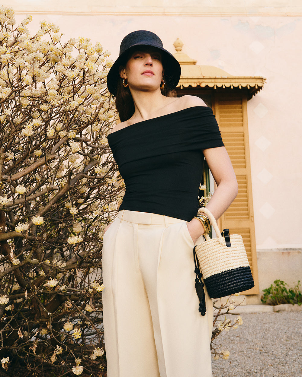 Person wearing an off-shoulder top and wide pants, carrying a woven handbag.