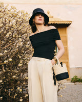 Person wearing an off-shoulder top and wide pants, carrying a woven handbag.