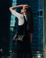 Person standing in city setting wearing a dress and holding a shoulder bag.