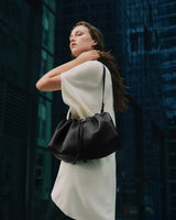 Person in a dress holding a gathered bag, standing outdoors near tall buildings.
