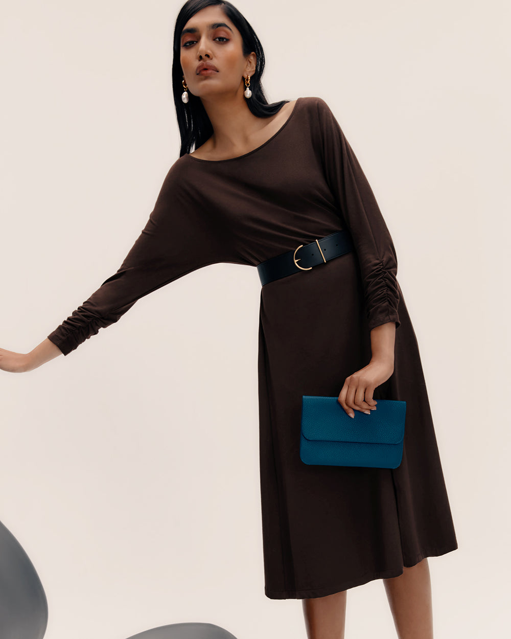 Person in a dress holding a clutch, standing and leaning slightly.