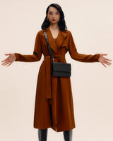 Person wearing a long coat and a shoulder bag, standing with arms slightly outstretched.