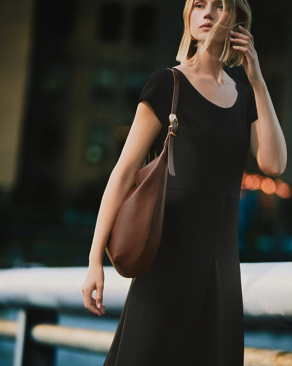 Person in dress holding a shoulder bag outdoors.