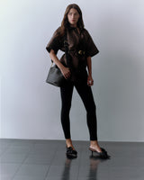 Person wearing a cape, leggings, slide sandals, carrying a croc-embossed leather travel bag