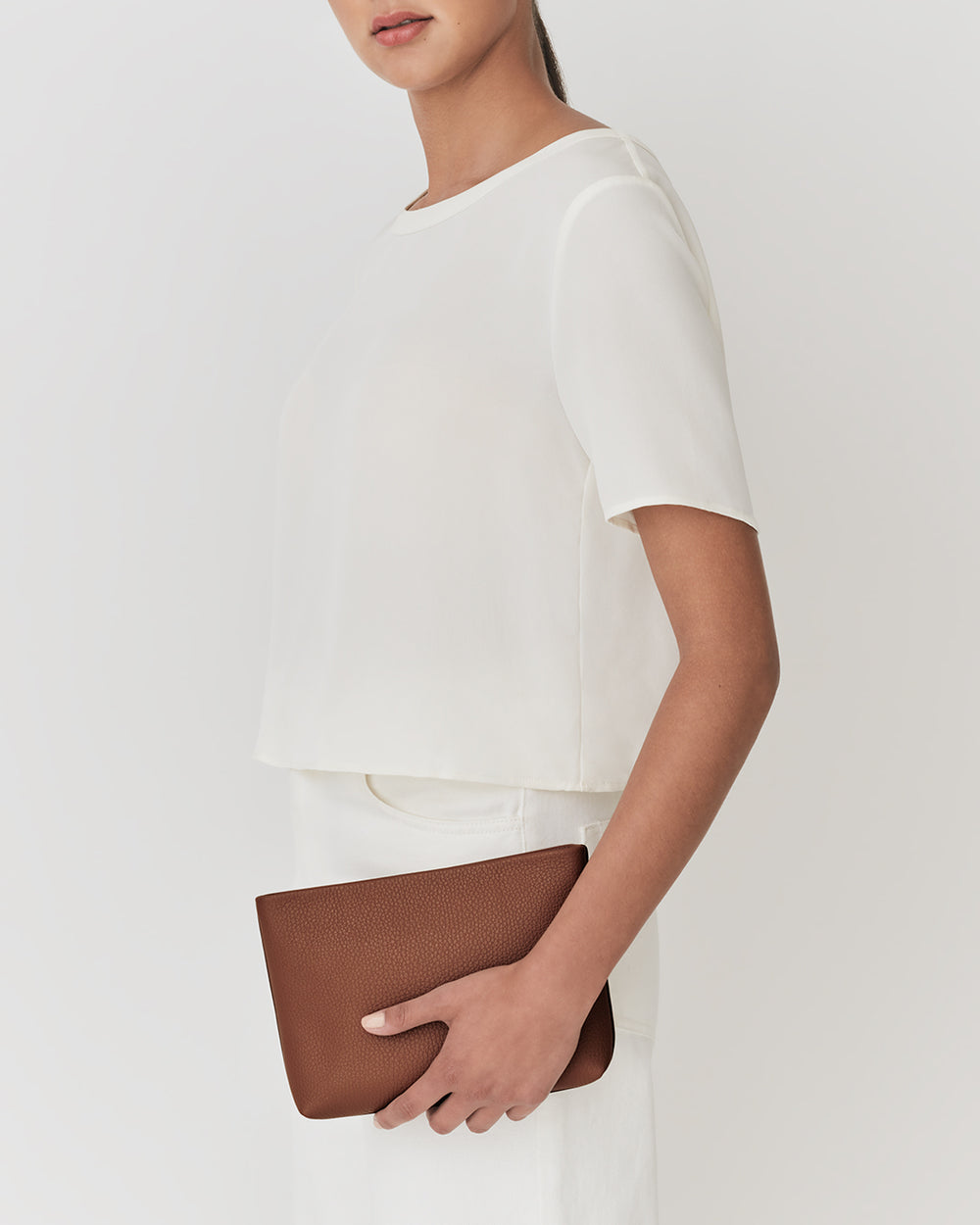 Person holding a pouch wearing a short-sleeved top and skirt.