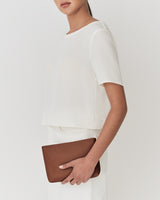 Person holding a pouch wearing a short-sleeved top and skirt.