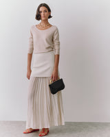 Woman in long skirt and top holding a small clutch bag