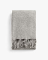 Folded blanket with fringed edges on a plain background.