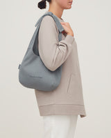 Person standing sideways holding a backpack over one shoulder.