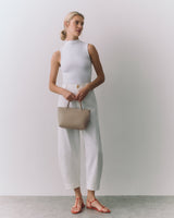 Person wearing sleeveless top and wide pants holds handbag, standing in sandals.