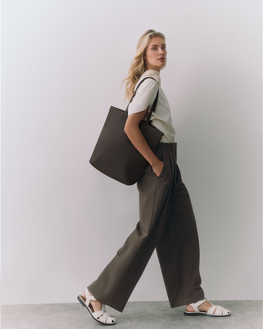 Person carrying a shoulder bag, wearing a t-shirt, wide-leg pants, and sandals