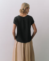 Person standing with back to camera wearing a short-sleeve top and a long skirt