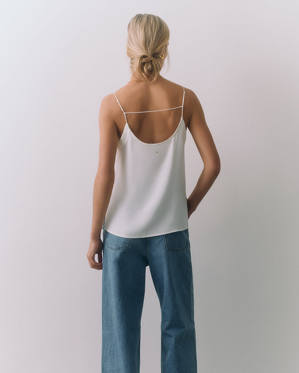 Person wearing a silk cami and jeans, facing away.