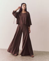 Person wearing loose top and wide-leg pants standing against plain backdrop