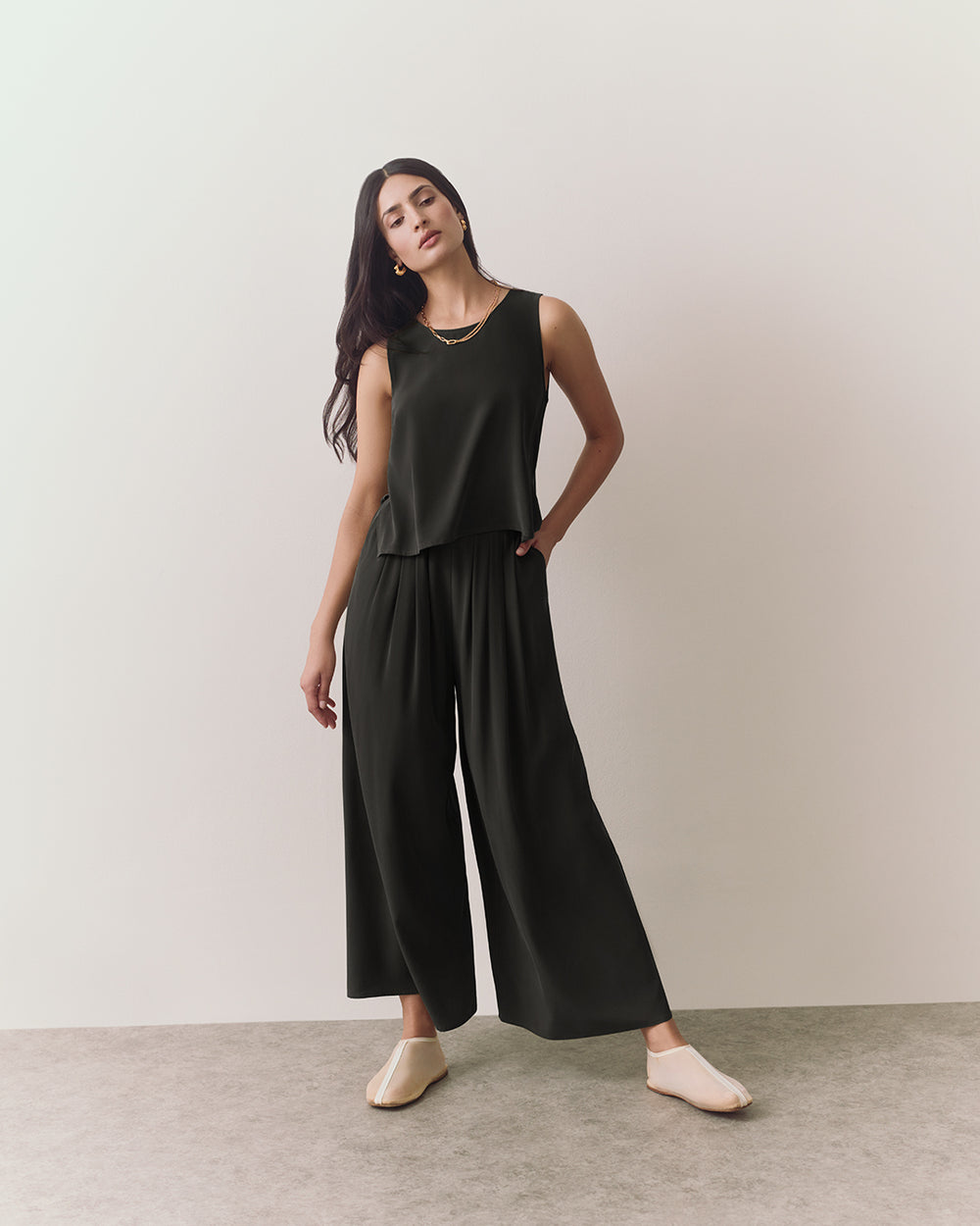 Person wearing a sleeveless top and wide-leg pants, standing on a plain background