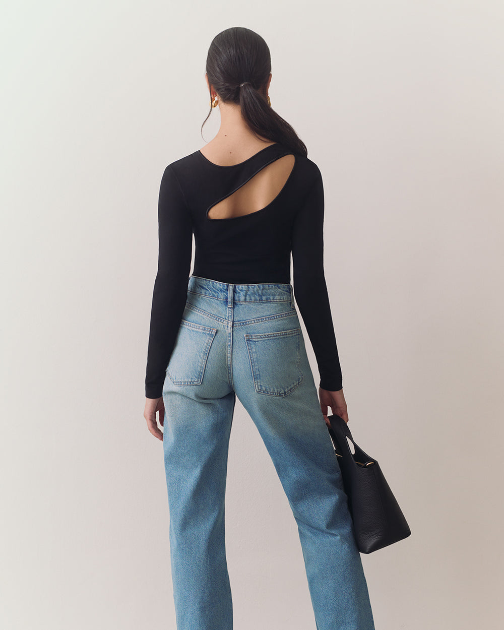 Person facing away, wearing open-back top and jeans, holding handbag.