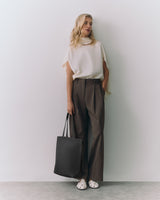 Person in a top and pants standing with a tote bag and looking left
