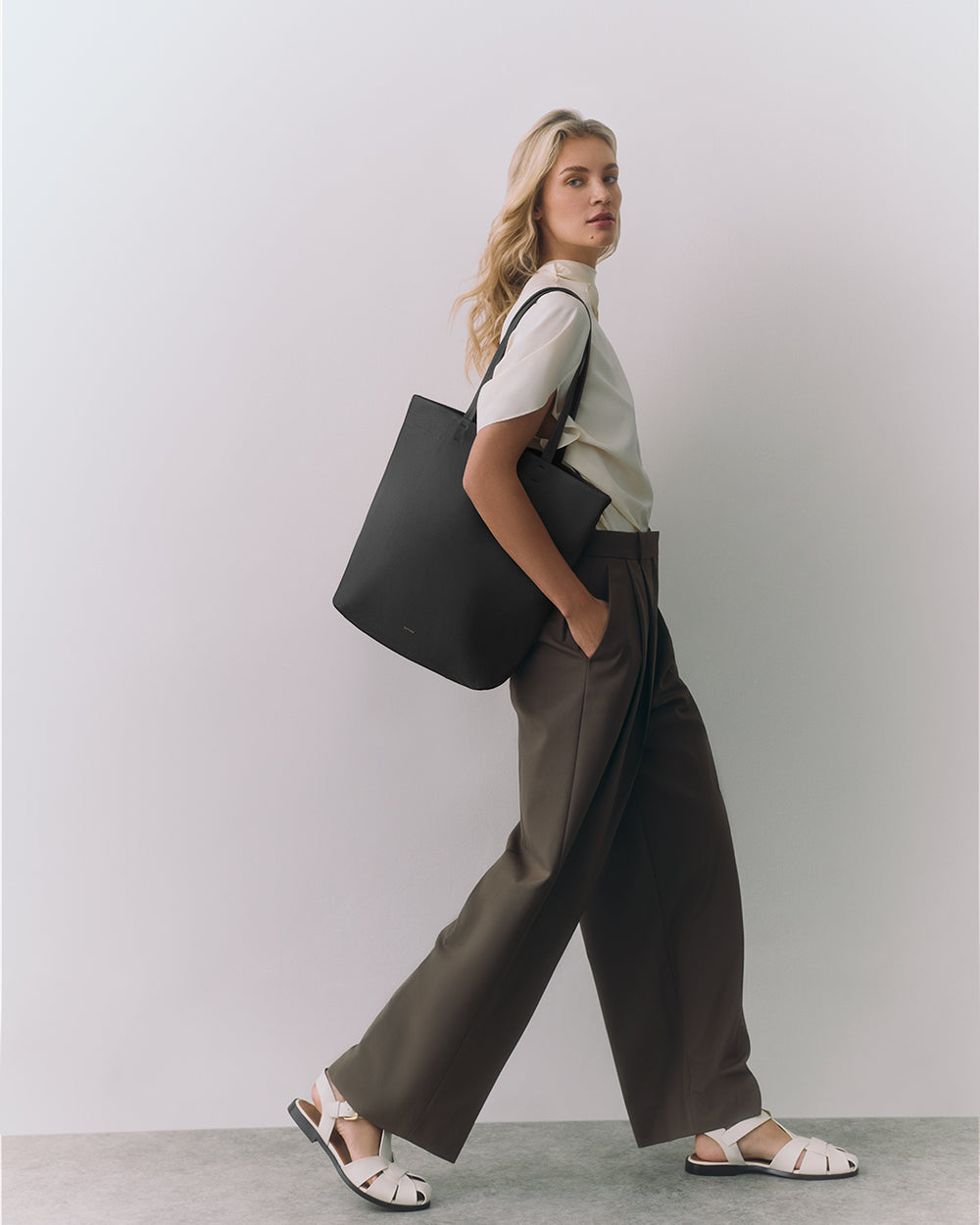 Person standing with a large tote bag over shoulder wearing wide-leg pants and sandals